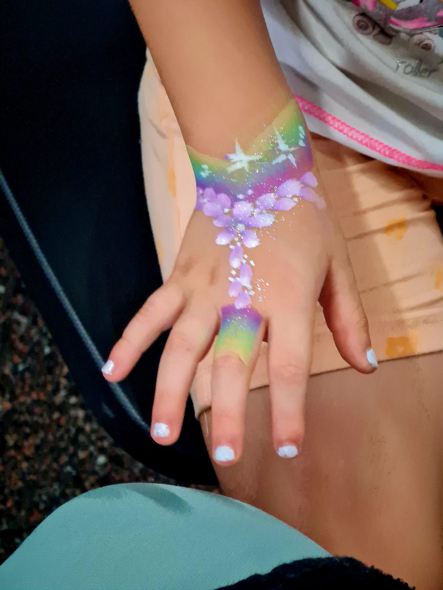 Pintura en mano y muñeca con arcoíris, flores y purpurina